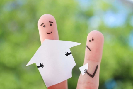 two fingers with faces drawn on them and one is holding a paper house