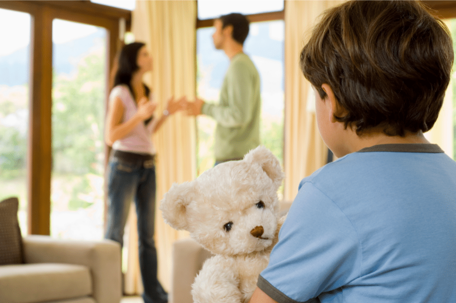 a child holding a bear watching his parents fight.