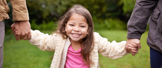 a child holding on to two peoples hands.